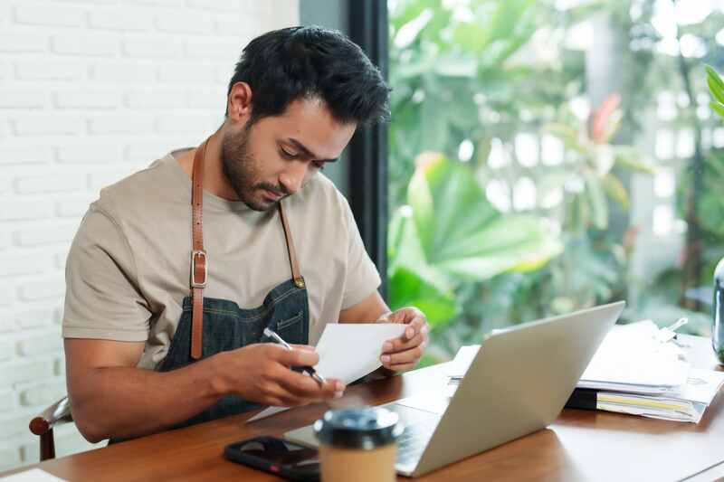 propriétaire d'un café utilisant un ordinateur portable pour vérifier des documents financiers