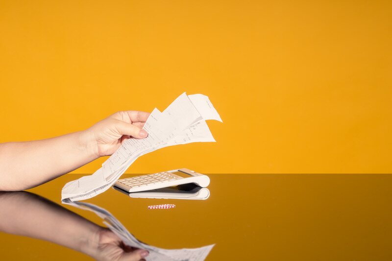 les mains chargées d'une pile de reçus et d'une calculatrice