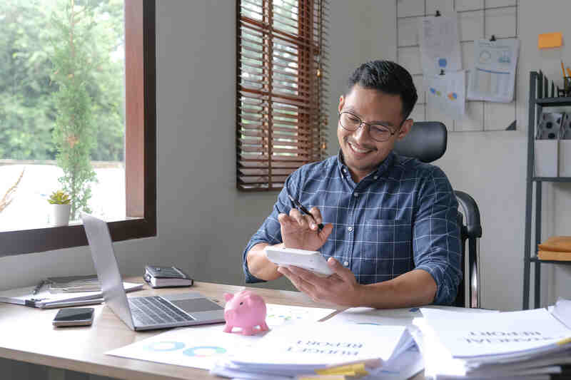 Hombre propietario de una pequeña empresa utilizando una calculadora y un ordenador portátil