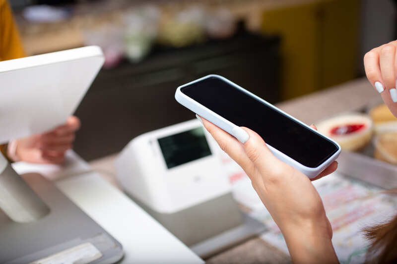 Vista de una persona sosteniendo un teléfono móvil en la caja registradora de una tienda minorista.