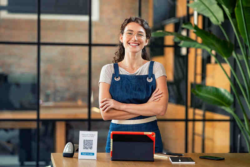 Propriétaire d'une petite entreprise prospère, debout devant la caisse enregistreuse, souriant