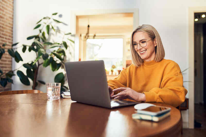 Happy woman using laptop while working remotely from home in living room