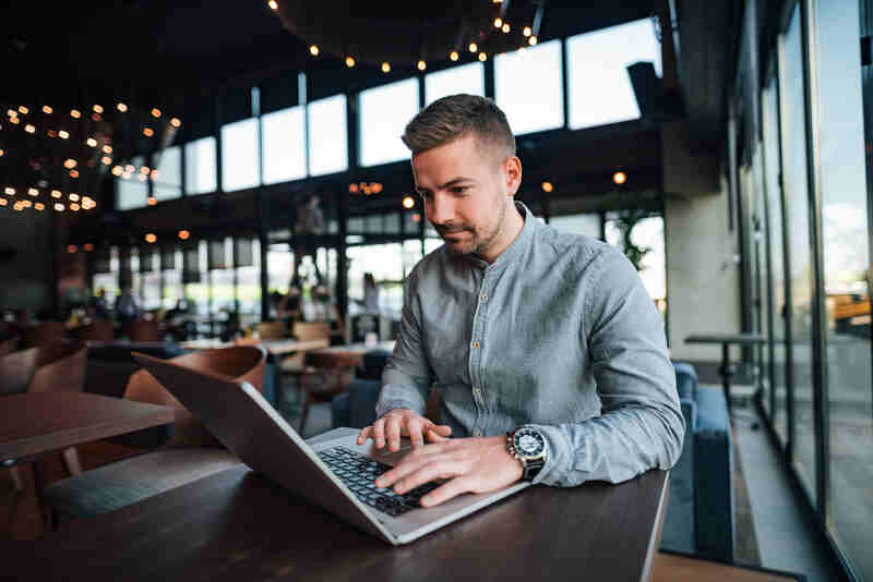 Young freelancer working on laptop in modern cafe