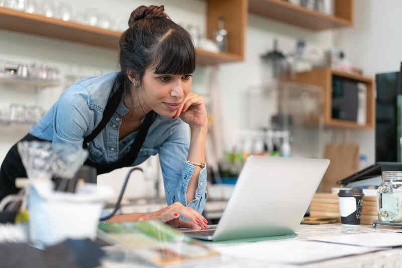 pequeña empresa dueña de una cafetería con delantal comprobando el pedido online de un cliente en el ordenador 